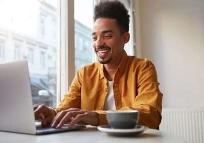 photo-young-attractive-african-american-smiling-boy-sits-cafe-works-laptop-drinks-aromatic-coffee-chatting-with-his-girlfriend-enjoy-freelance-work_295783-2433